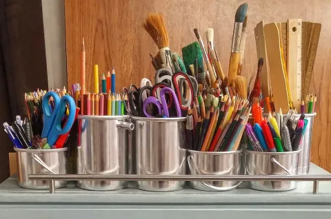 Art supplies in silver containers in a row.