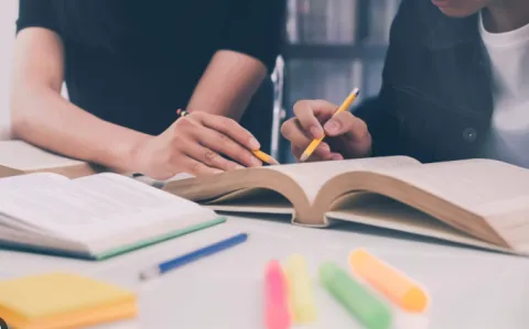 two people studying a book with pencils and highlighters