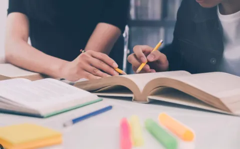 two people studying a book with pencils and highlighters